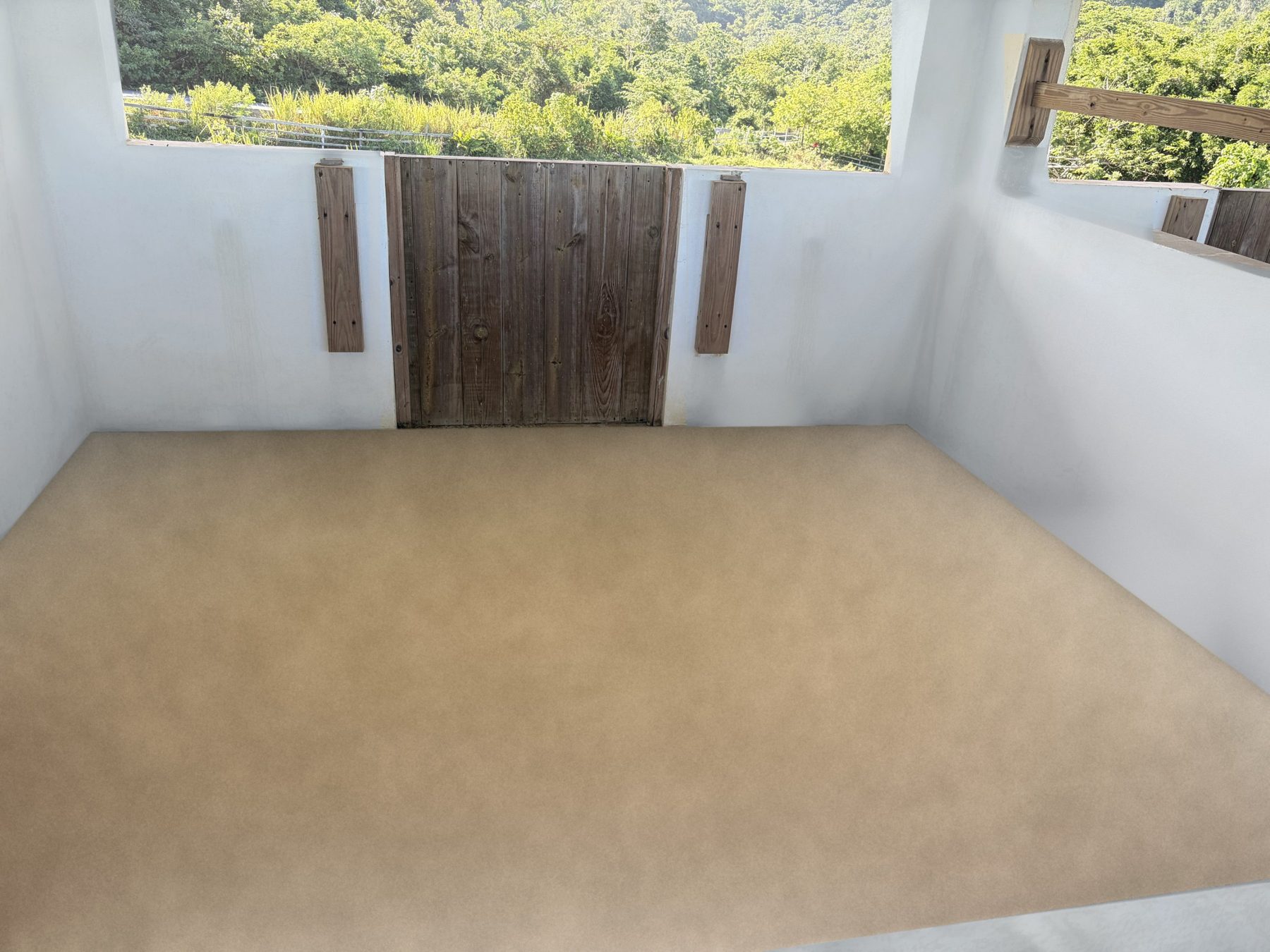 Inside an open-air studio with white walls, a wooden shutter and a view of green hills